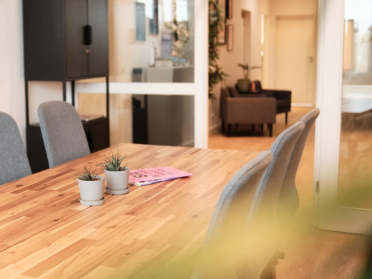Moderner Besprechungsraum und Arbeitsatmosphäre – wemotion Digitalagentur Moderner Besprechungsraum der wemotion Digitalagentur mit Holztisch, grauen Stühlen und Pflanzen – einladende Arbeitsumgebung.