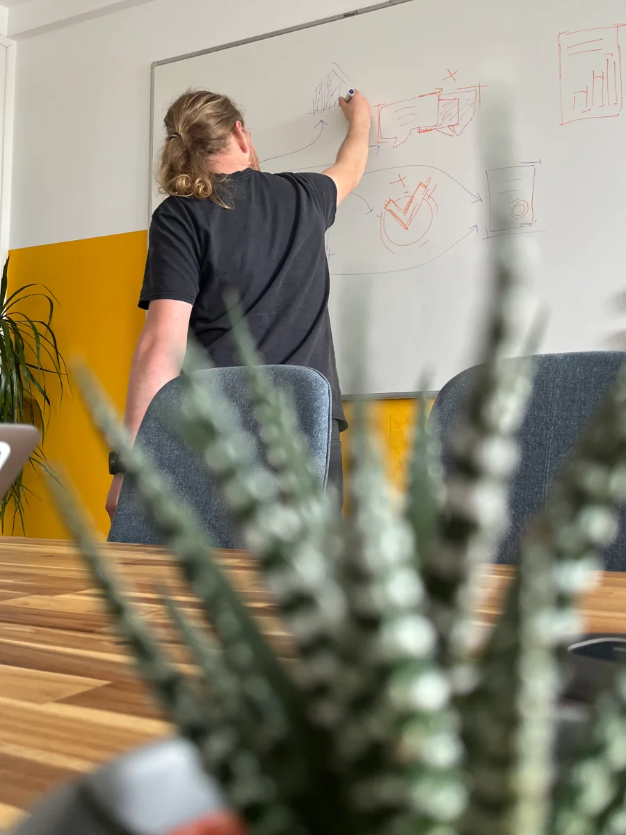 Person skizziert Marken- und Designideen auf einem Whiteboard in einem modernen Besprechungsraum – Symbol für kreative Markenentwicklung bei der wemotion Digitalagentur.