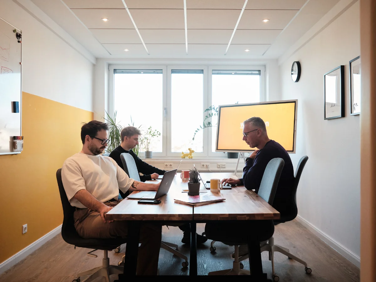 Gemeinsame Teamarbeit im Besprechungsraum – wemotion Digitalagentur Drei Mitarbeiter der wemotion Digitalagentur arbeiten gemeinsam konzentriert an Laptops in einem modernen Besprechungsraum.